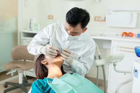photo of male asian dentist diong a dental check up to a young asian woman in a dentist officeの写真素材