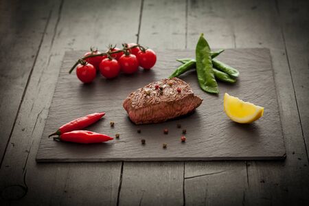 Delitious steak with vegetables over stone plateの写真素材