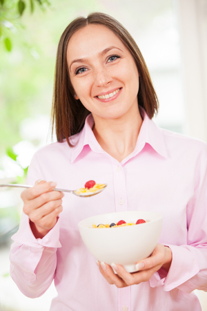 Portrait of smiling brunette woman holding a bowl with corn flakes with berries in her handsの写真素材