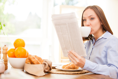 Brunette businesswoman is reading the newspaper while having breakfast at homeの写真素材