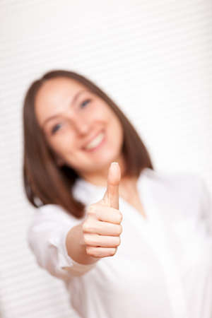 Smiling brunette businesswoman is making positive thumb gesture over white backgroundの写真素材