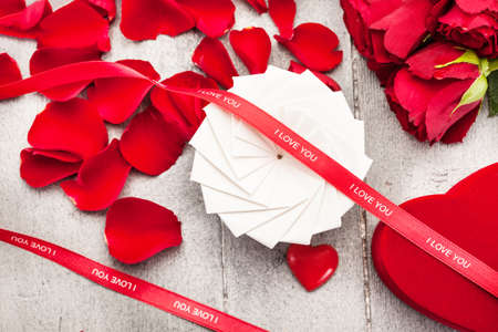 Photo of gift box, red roses and petals over wooden tableの写真素材