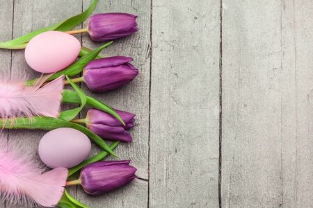 Top view of pink easter eggs and violet tulips over wooden tableの写真素材