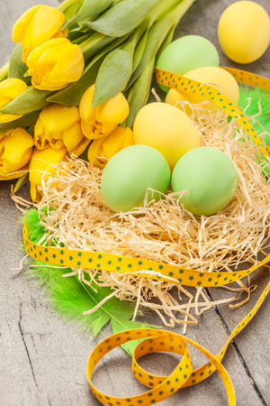 Photo of easter eggs and yellow tulips over wooden tableの写真素材