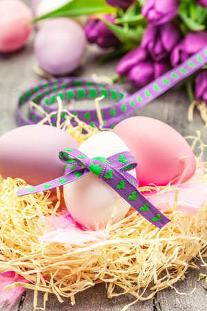 Photo of easter eggs and violet tulips over wooden tableの写真素材