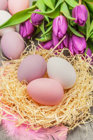 Photo of easter eggs and violet tulips over wooden tableの写真素材