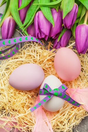 Photo of easter eggs and violet tulips over wooden tableの写真素材