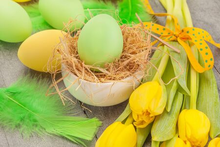 Photo of easter eggs and yellow tulips over wooden tableの写真素材