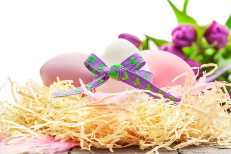 Photo of easter eggs and violet tulips over wooden tableの写真素材