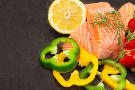 Photo of fresh tasty salmon with vegetables over black backgroundの写真素材