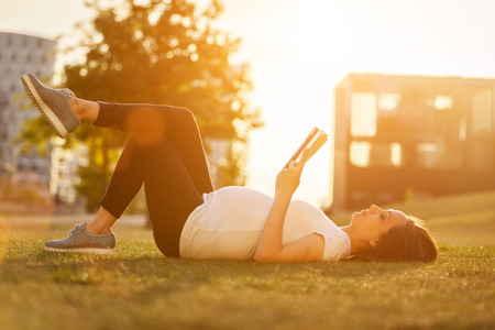 Photo of pregnant woman is reading a book on a green fieldの写真素材