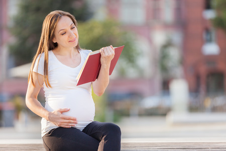 Photo of caucasian brunette pregnant woman reading the book on a benchの写真素材