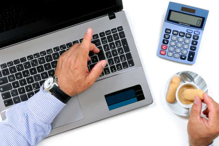 Top view of a man who eats breakfast with coffee and cookies on the desk in a modern office