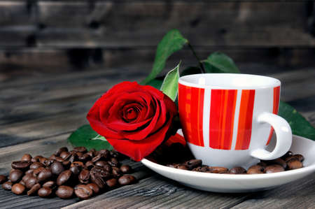Aromatic Italian style coffee served in a beautiful red cup on a wooden table old adorned with a red rose and coffee beans.の写真素材