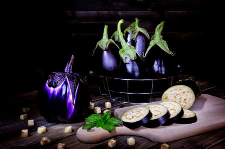 Close up of fresh purple whole eggplant and sliced over an aged wood table. Photographed with light painting technique.の写真素材