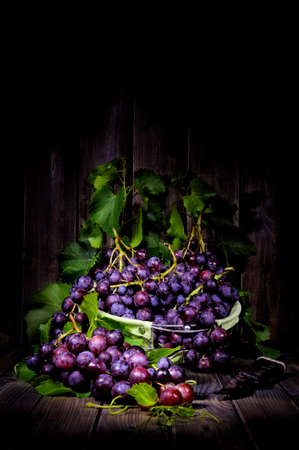 Fresh red grapes bunch lying on leaves on an old wooden table. Photographed with light painting techniqueの写真素材