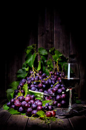Fresh red grapes bunch lying on leaves on an old wooden table. Photographed with light painting techniqueの写真素材