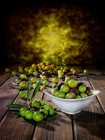 Close up of a bowl of fresh olives freshly picked on an antique wooden table.の写真素材