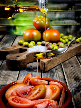 Close-up of an cruet pouring olive oil over tomato salad on an antique wooden tableの写真素材