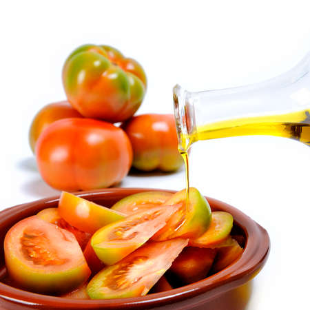 Close up of an ampoule pouring olive oil on a fresh tomato salad isolated on white backgroundの写真素材