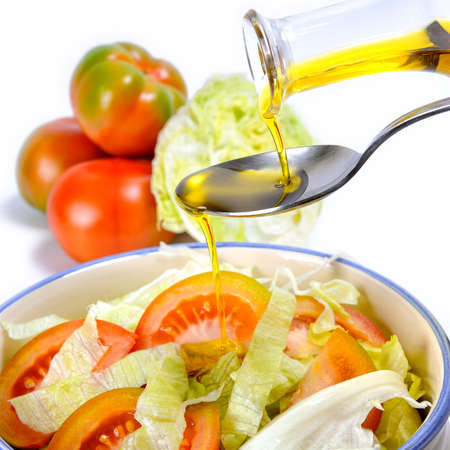 Close-up of an ampoule pouring olive oil on a fresh salad of tomatoes and vegetables isolated on white backgroundの写真素材