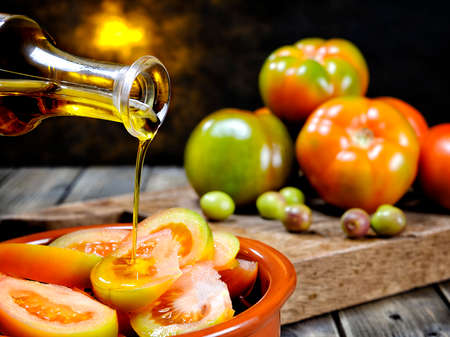 Close-up of an cruet pouring olive oil over tomato salad on an antique wooden tableの写真素材