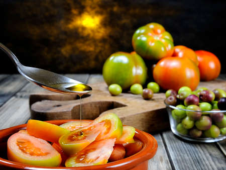Close-up of a spoon pouring olive oil on a salad of tomatoes on an antique wooden tableの写真素材