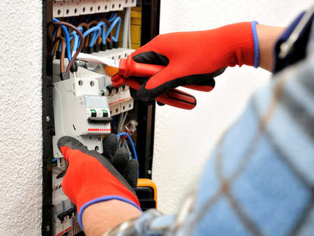 Young electrician technician introduces the electric cable into the clamp of the magnetothermic...