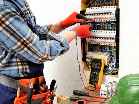 Young electrician technician measures with a multimeter the voltage in a electrical panelの写真素材