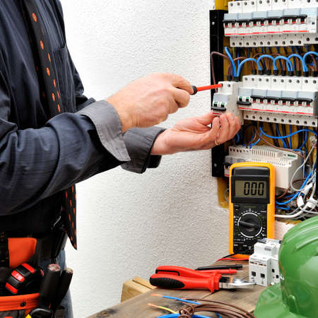 Elegant technical electrician fixing the cable into the terminal of a circuit breaker of a residential electrical panelの写真素材