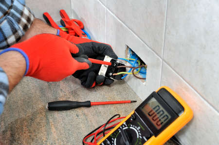 Electrician technician with gloves and safety instruments fixes the electric cable to the socket of a residential installation.の写真素材