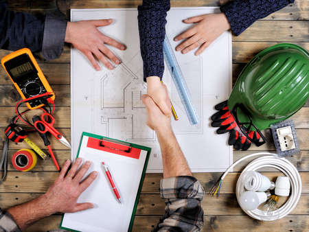 top view of young engineers and a technician studying a residential construction project on an antique wooden tableの写真素材