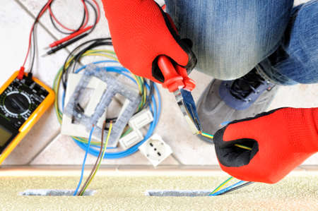 Electrician technician at work with pliers on the cable of in a residential electric installationの写真素材