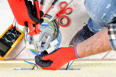 Electrician technician at work with pliers on the cable of in a residential electric installationの写真素材
