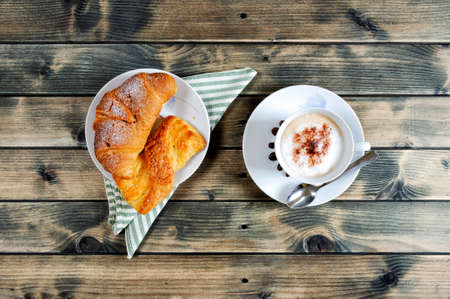 Top view of a cup of coffee with milk, croissant and brioche on an antique wooden table.の写真素材