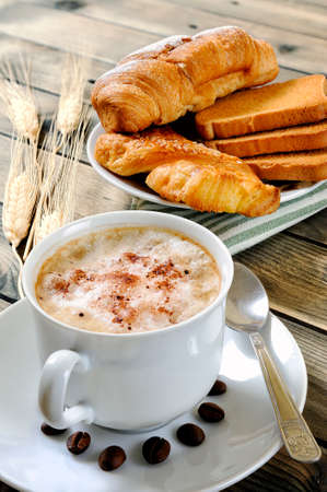 Close-up of a cup of coffee with milk, croissant, brioche and rusks on an antique wooden table.の写真素材