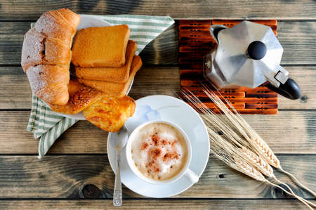 Top view of a cup of coffee with milk, croissants, brioche, rusks and the coffee pot on an antique wooden table.の写真素材