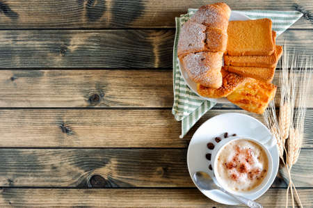 Top view of a cup of coffee with milk, croissants, brioche and rusks on an antique wooden table.の写真素材