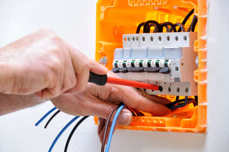 Electrician technician working on a residential electrical panel, fixing with a screwdriver the cable in the magnetothermal switchの写真素材