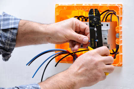 Electrician technician at work on a residential electric panel, prepares the cable with a wire strippersの写真素材