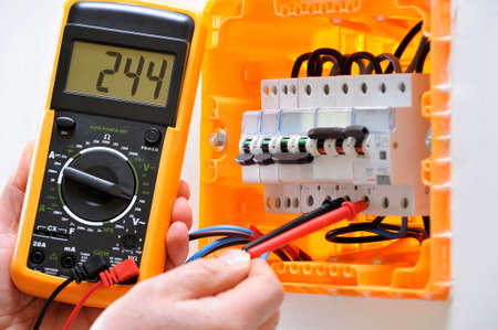 Electrician technician working on a residential electrical panel, measures the voltage on the terminals of the thermal magnetic circuit breakerの写真素材