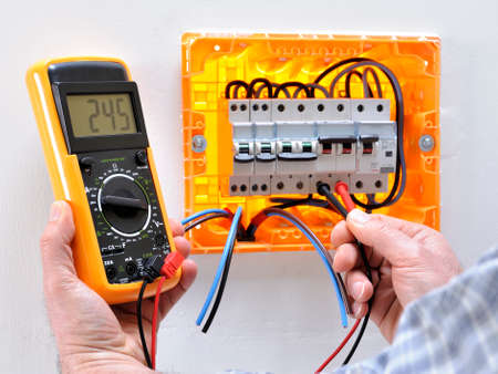 Electrician technician working on a residential electrical panel, measures the voltage on the terminals of the thermal magnetic circuit breakerの写真素材
