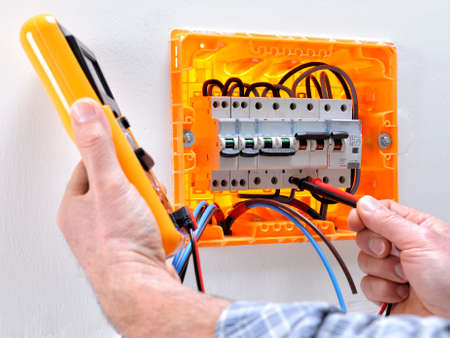 Electrician technician working on a residential electrical panel, measures the voltage on the terminals of the thermal magnetic circuit breakerの写真素材