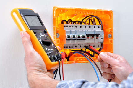 Electrician technician working on a residential electrical panel, measures the voltage on the terminals of the thermal magnetic circuit breakerの写真素材