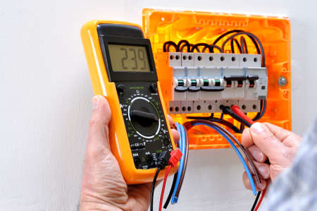 Electrician technician working on a residential electrical panel, measures the voltage on the terminals of the thermal magnetic circuit breakerの写真素材
