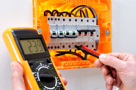Electrician technician working on a residential electrical panel, measures the voltage on the terminals of the thermal magnetic circuit breakerの写真素材