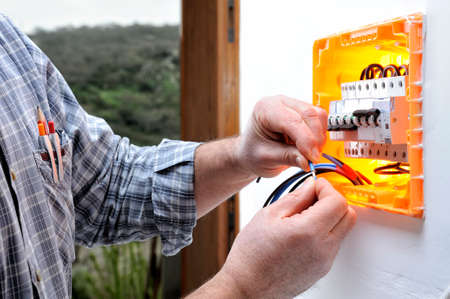Electrician technician at work on a residential electric panel, prepares the wire with his handsの写真素材