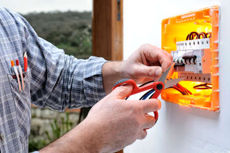 Electrician technician at work on a residential electric panel, cuts the wire with scissorsの写真素材