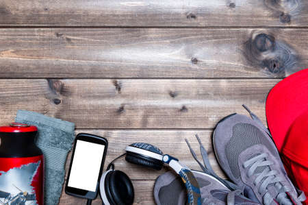 Top view of sport shoes, sound headphone, smartphone, hat, towel and water bottle photographed on an antique wooden table. Text space.の写真素材