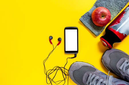 Top view of a red apple, sport shoes, audio headphone, smartphone, towel and water bottle...